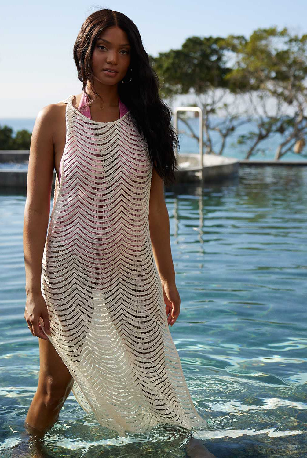 A woman wearing an ivory sleeveless cover up with scalloped lace detailing standing in a pool.