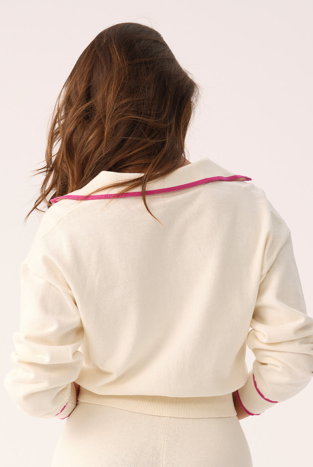 Woman wearing a white sweater and shorts with pink trim on a plain background