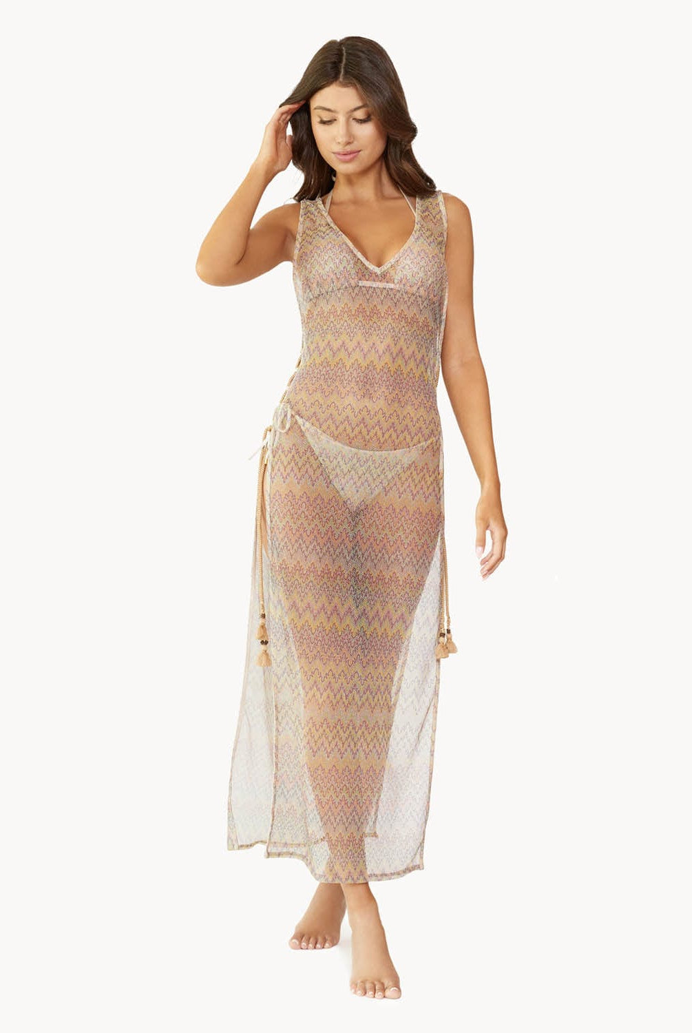 Brunette woman wearing a multi-colored sleeveless lace tunic with open side slits and lace-up side details with tassel tie ends over a matching bikini stands in front of white wall.