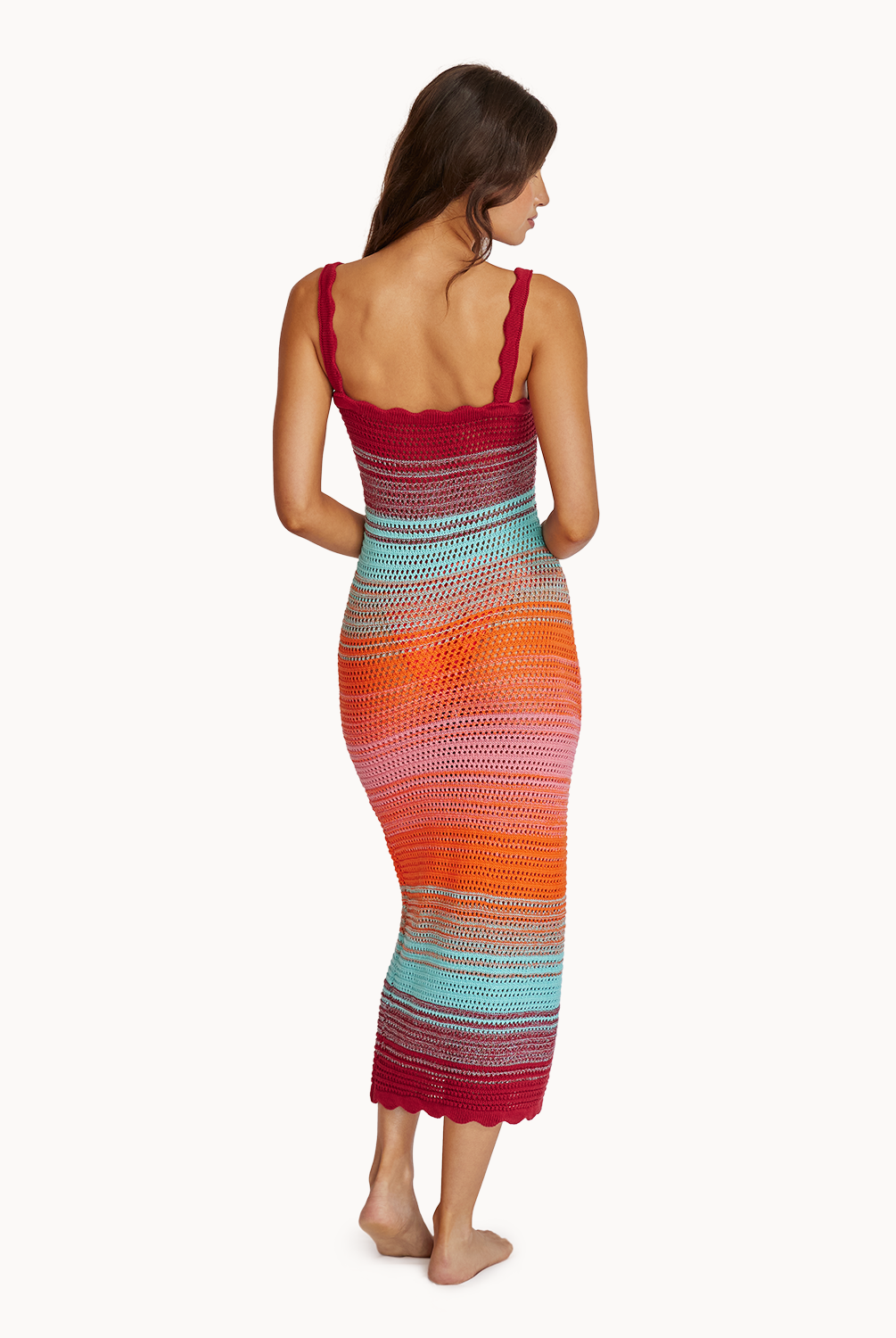 A woman wearing a midi length knit dress facing towards a white wall.