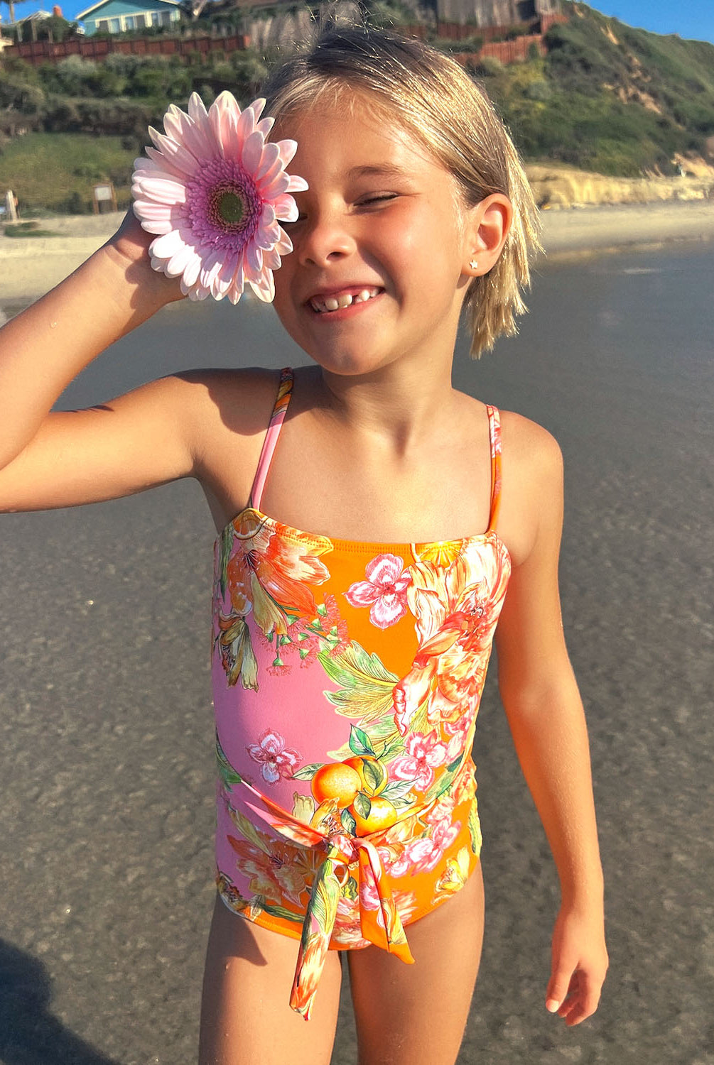 A young girl wearing a floral one piece swim suit standing on a beach near an ocean.