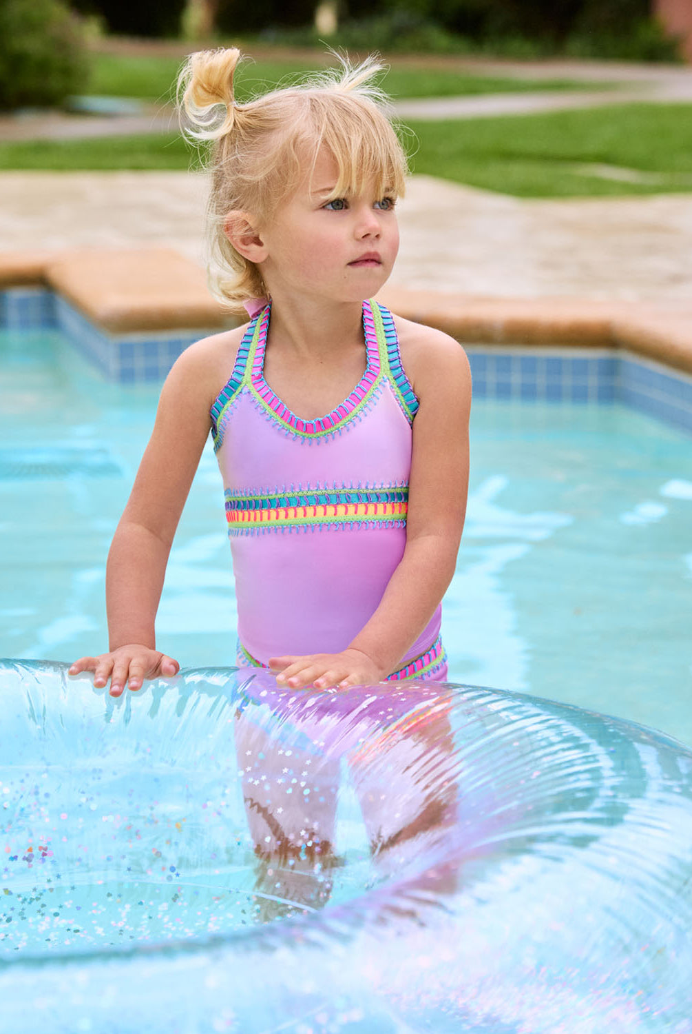 A blonde girl wearing a pink tankini swimsuit playing in the pool with a blow up inner tube.