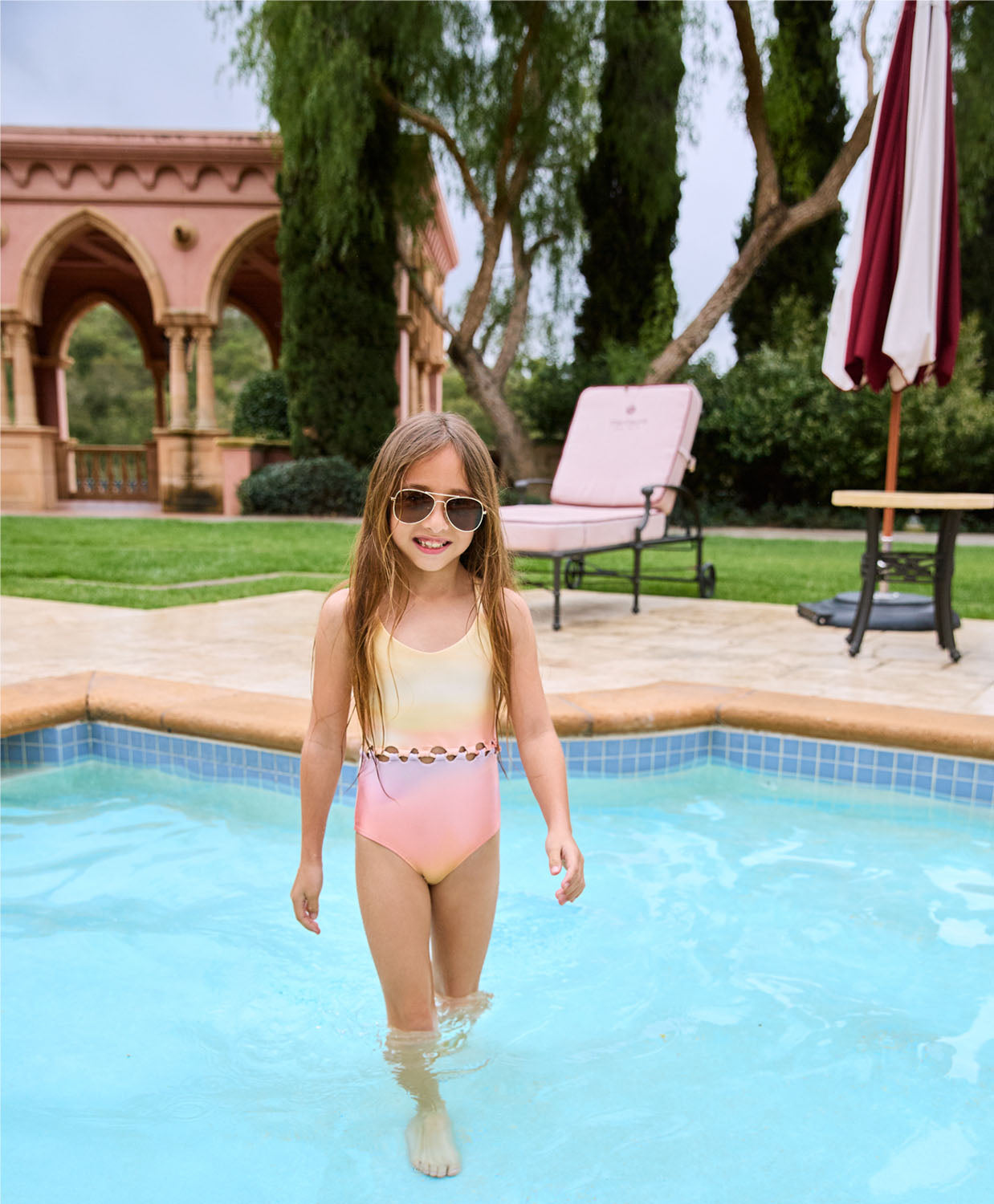 A brunette girl wearing a color one piece swimsuit standing in a pool.