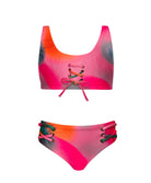 A pink tie dye kids bikini against a white wall.