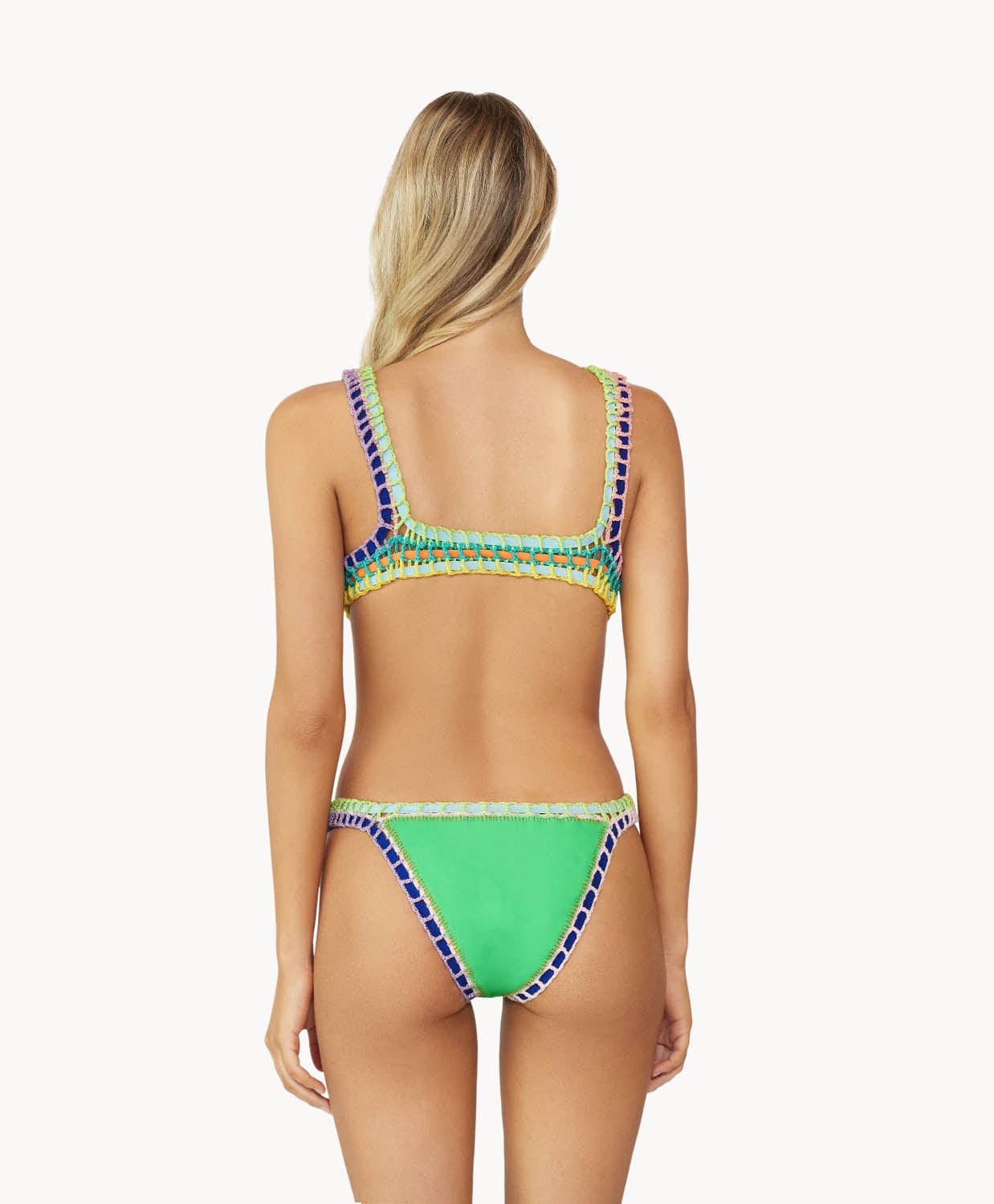 A blonde woman wearing a green bikini facing towards a white wall.