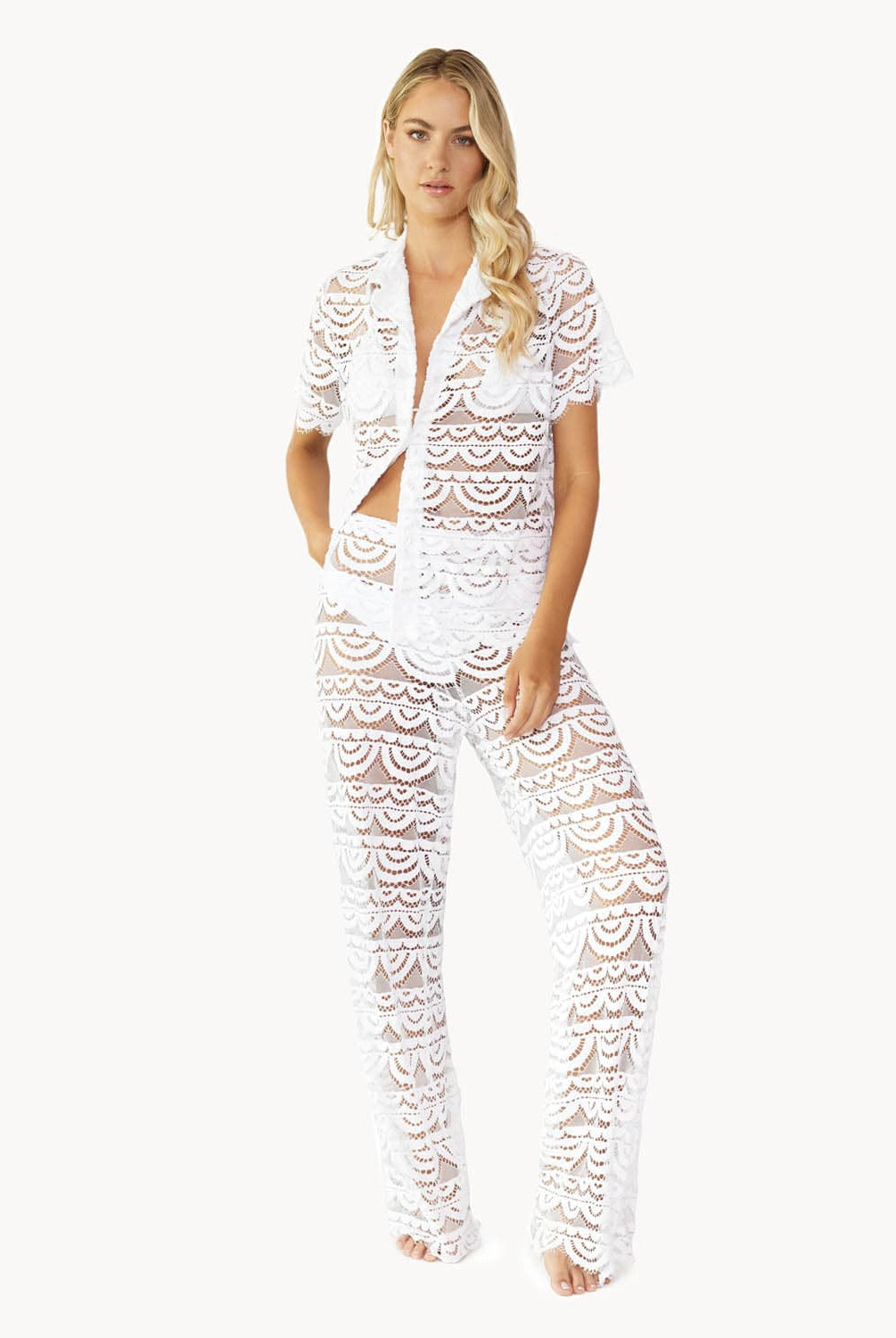 Woman wearing a matching white lace button shirt and pant against white wall.