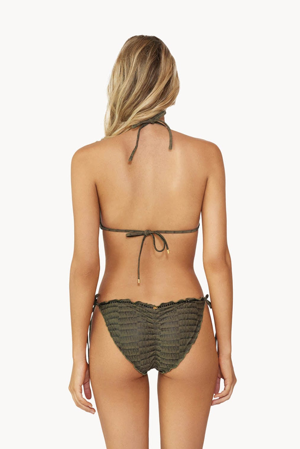 Blonde woman wearing a textured gray triangle shape bikini with ruffle details facing backwards towards a white wall.