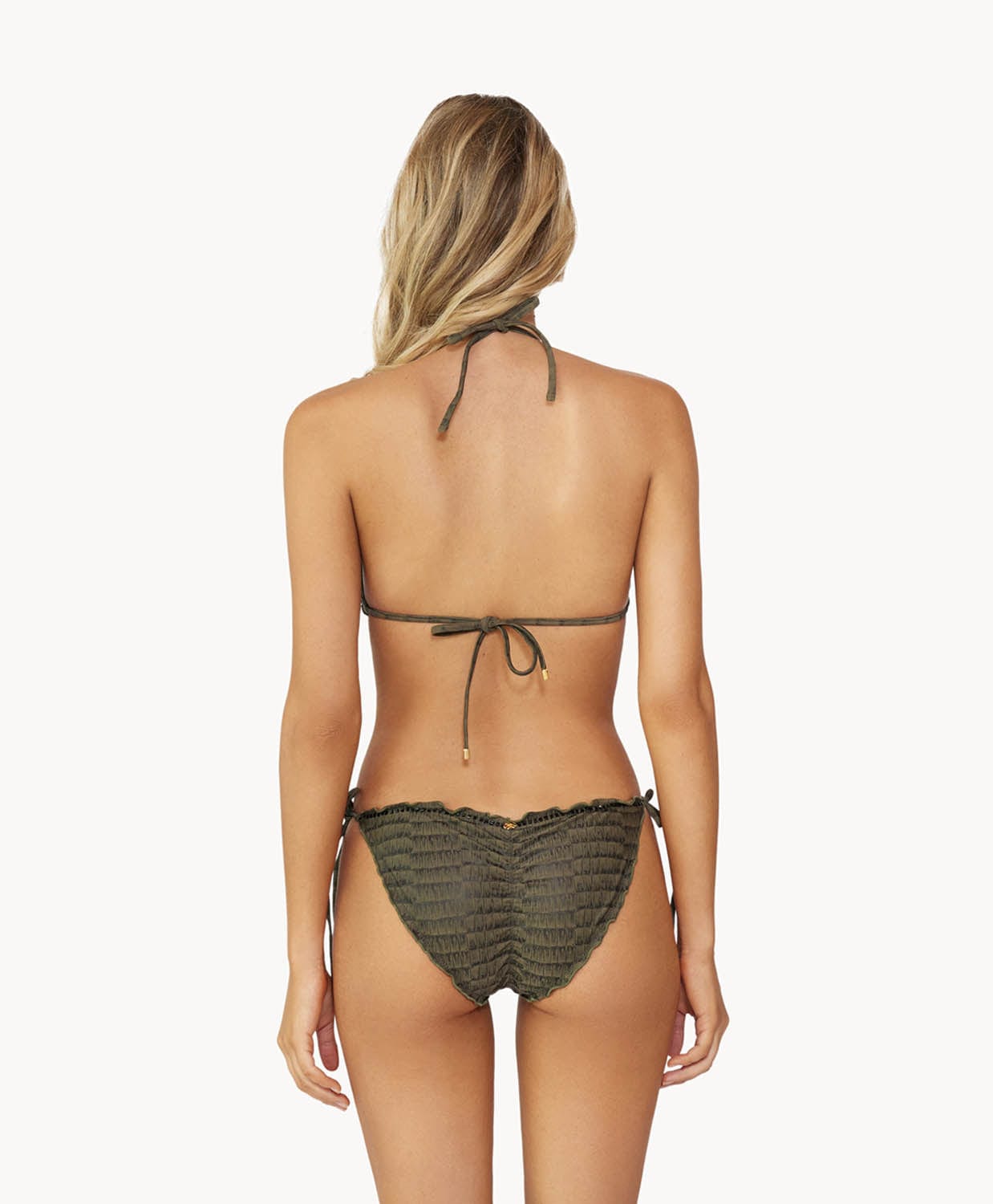 Blonde woman wearing a textured gray triangle shape bikini with ruffle details facing backwards towards a white wall.