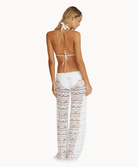 Back view of woman wearing white lace pants in front of a white background.