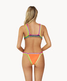 A blonde woman wearing an orange bikini facing towards a white wall.