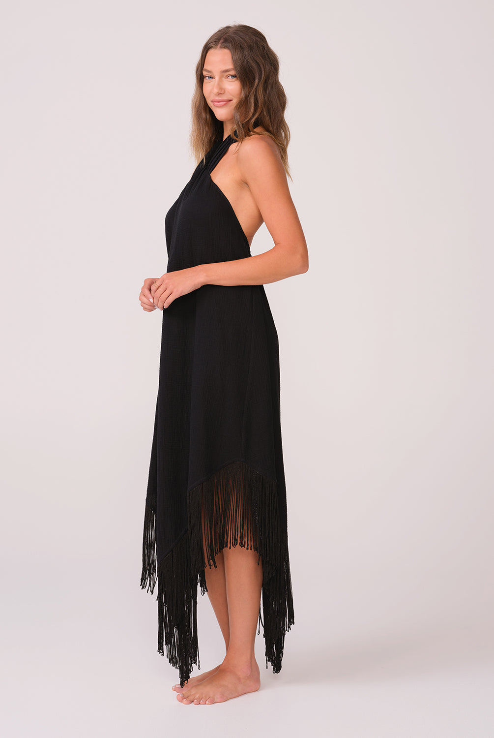 A woman wearing a long black fringe dress standing against a white wall.
