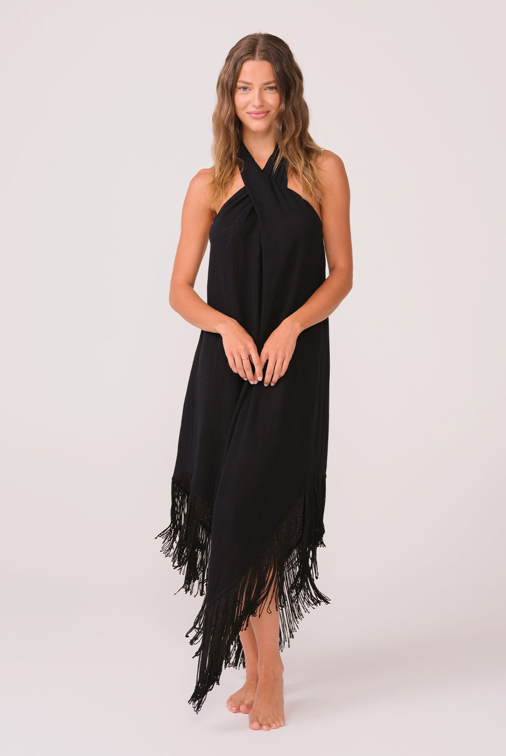 A woman wearing a long black fringe dress standing against a white wall.