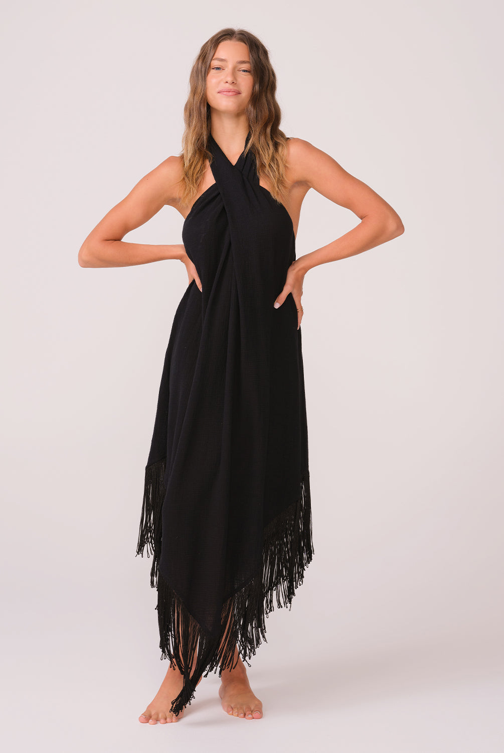 Woman wearing a black long fringe dress standing against a white wall.