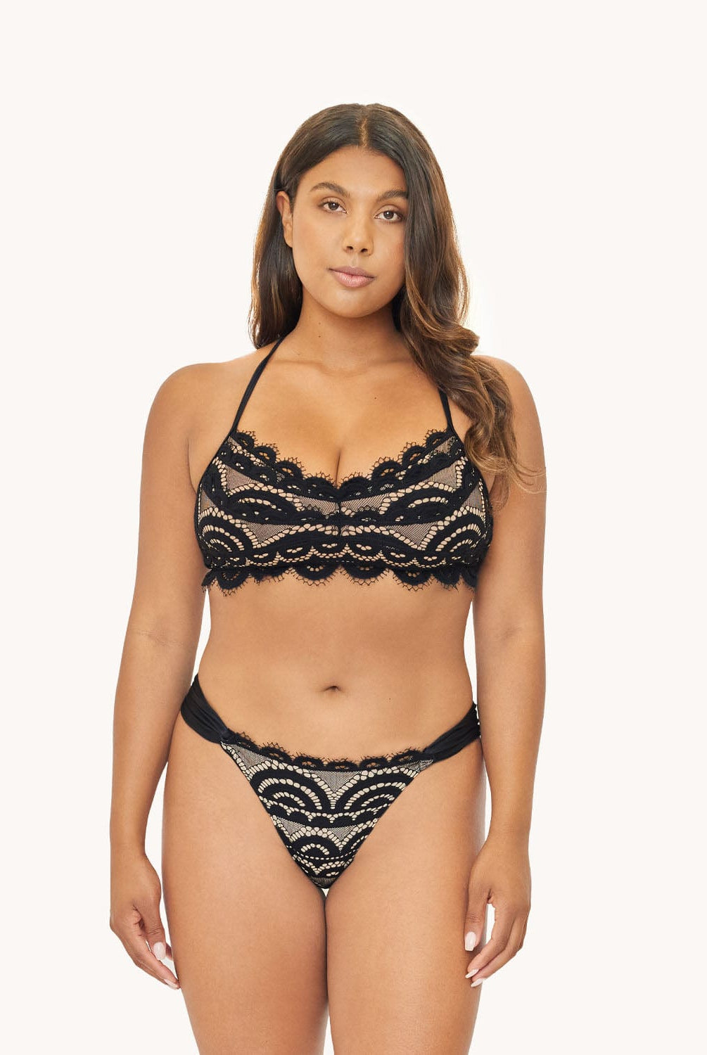 Woman in black lace bikini against white wall.