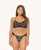 Woman in black lace bikini against white wall.