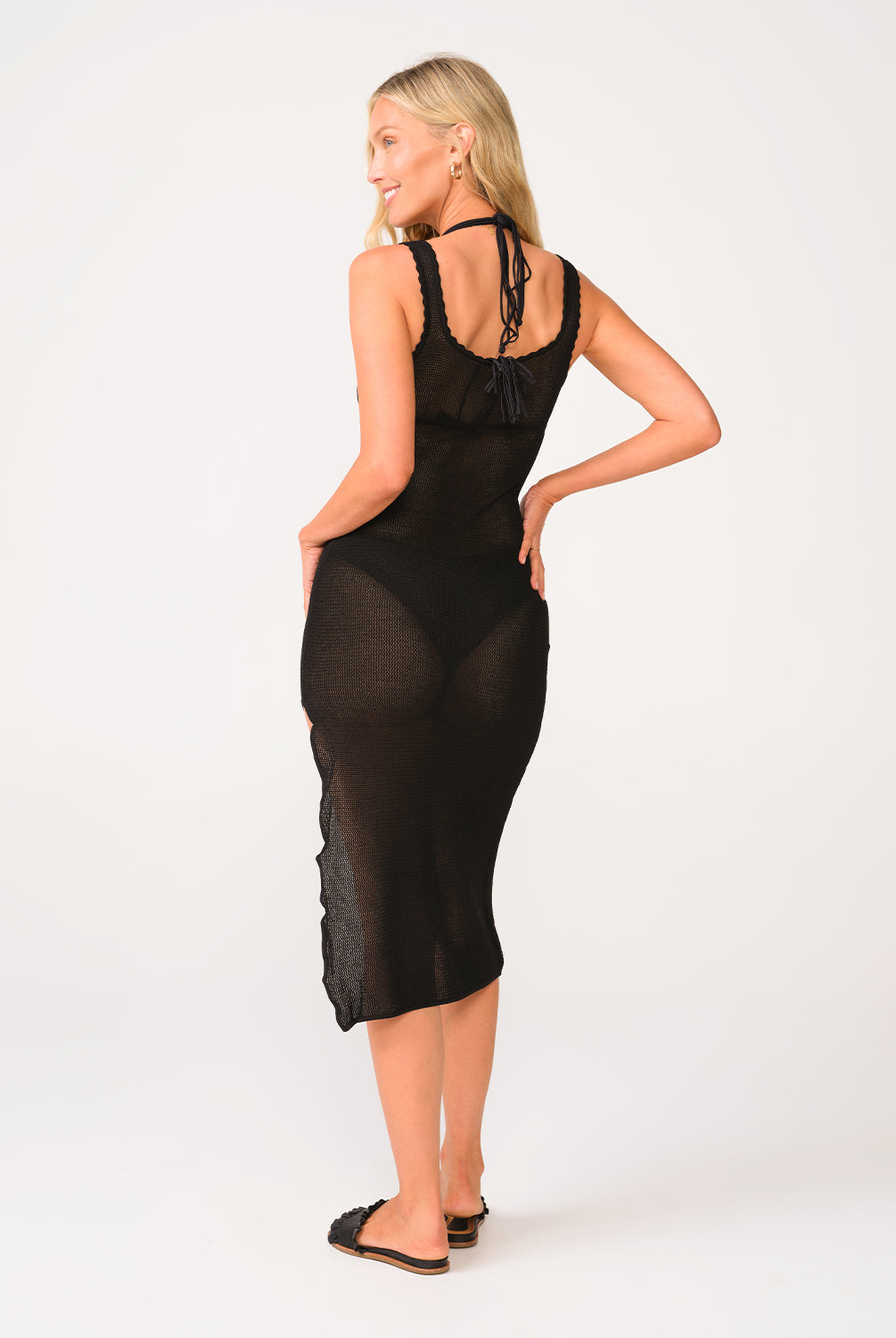 A woman wearing a black midi dress standing against a white wall.