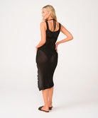 A woman wearing a black midi dress standing against a white wall.
