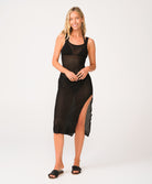 A woman wearing a black midi dress standing against a white wall.