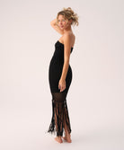 Woman wearing a black strapless dress with fringe details on a white background