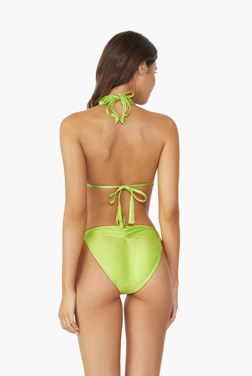Brunette woman wearing a lime macrame triangle shape bikini facing backwards towards white wall.