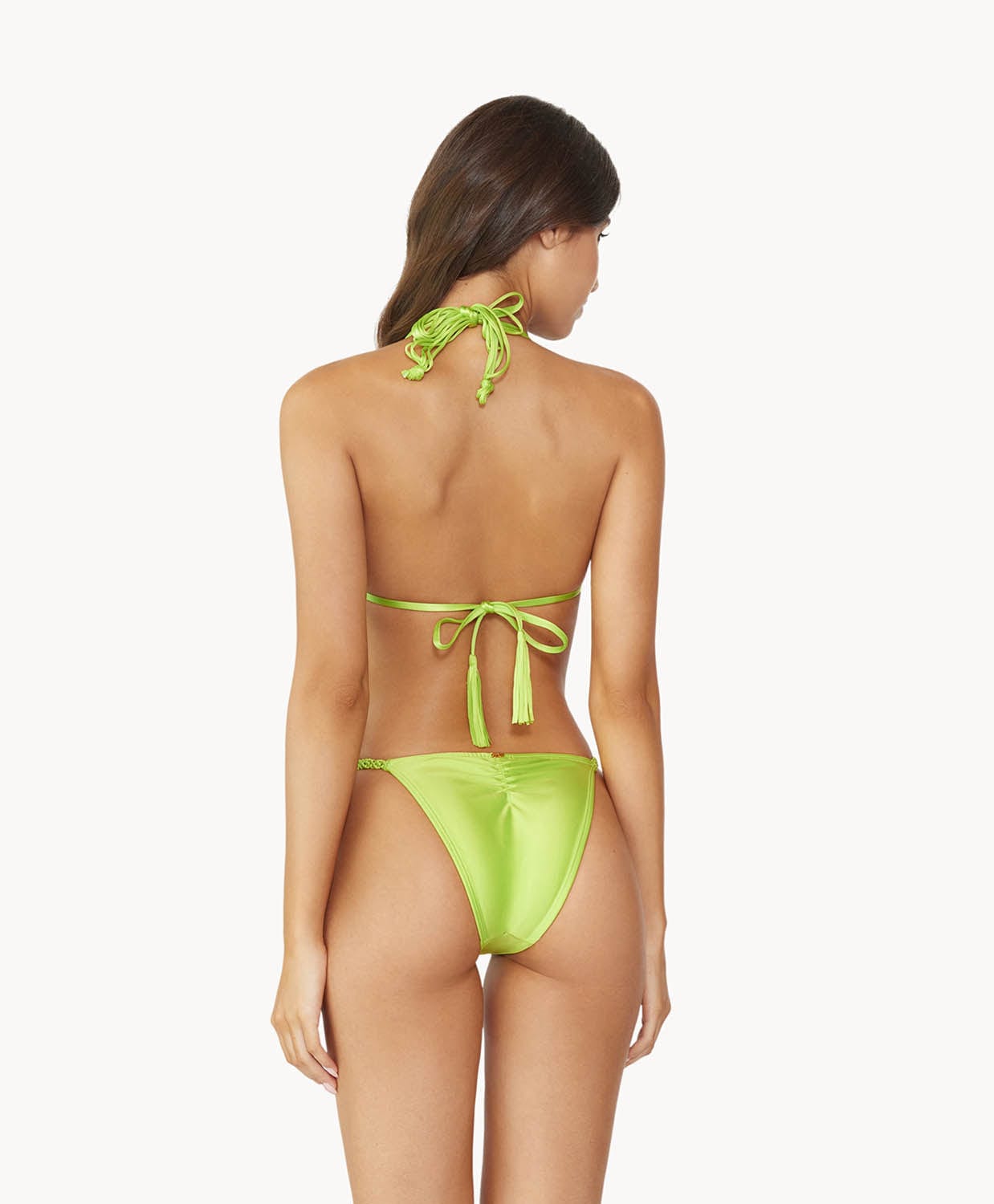 Brunette woman wearing a lime macrame triangle shape bikini facing backwards towards white wall.