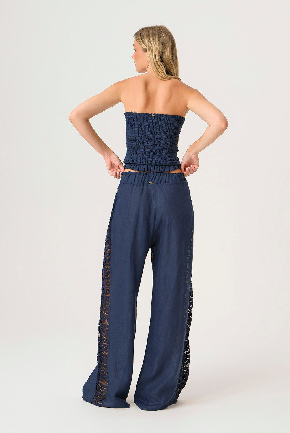 Woman wearing a navy strapless top and wide-leg pants with lace details on a white background