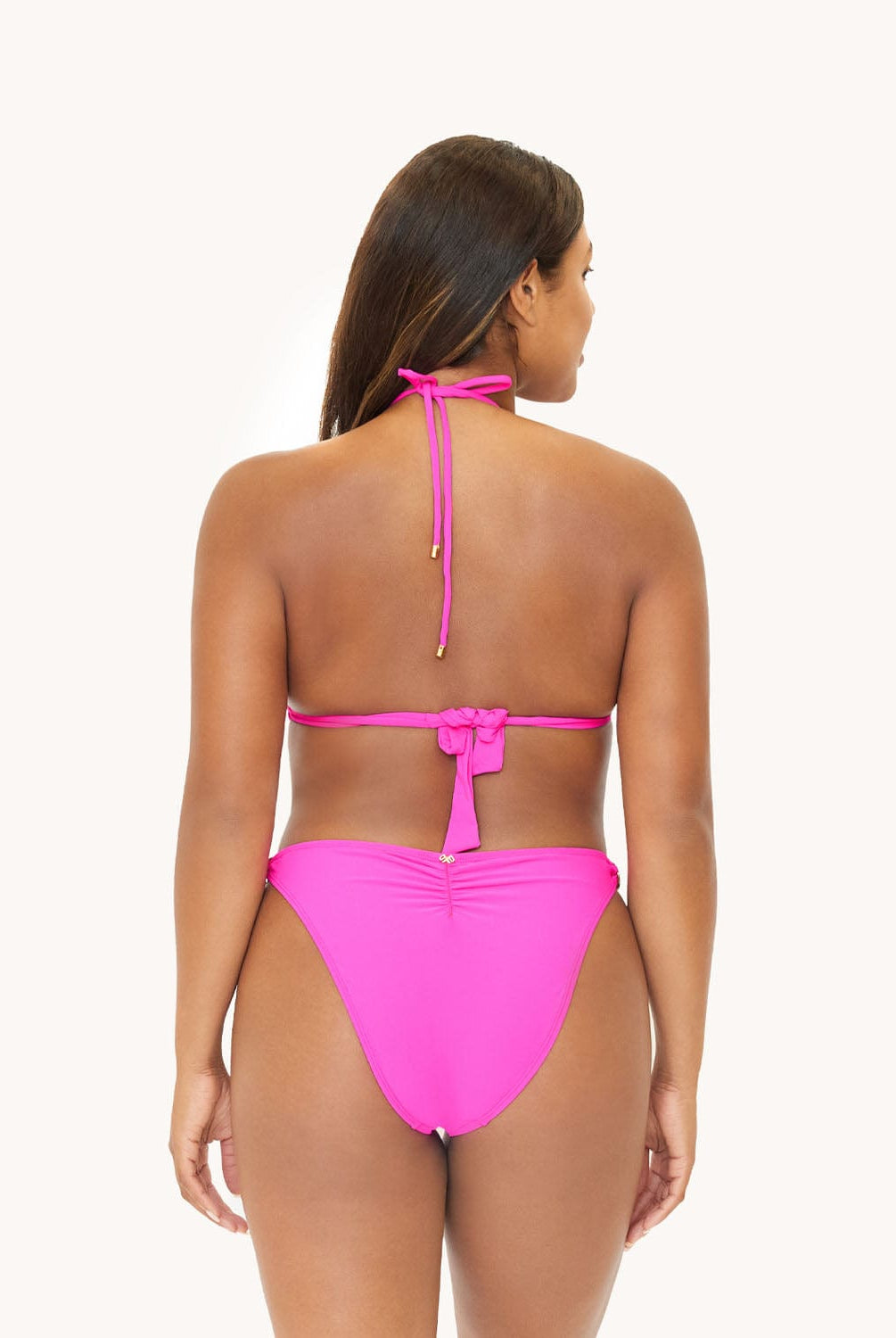 Back view of brunette woman wearing a neon pink bikini in front of a white background.