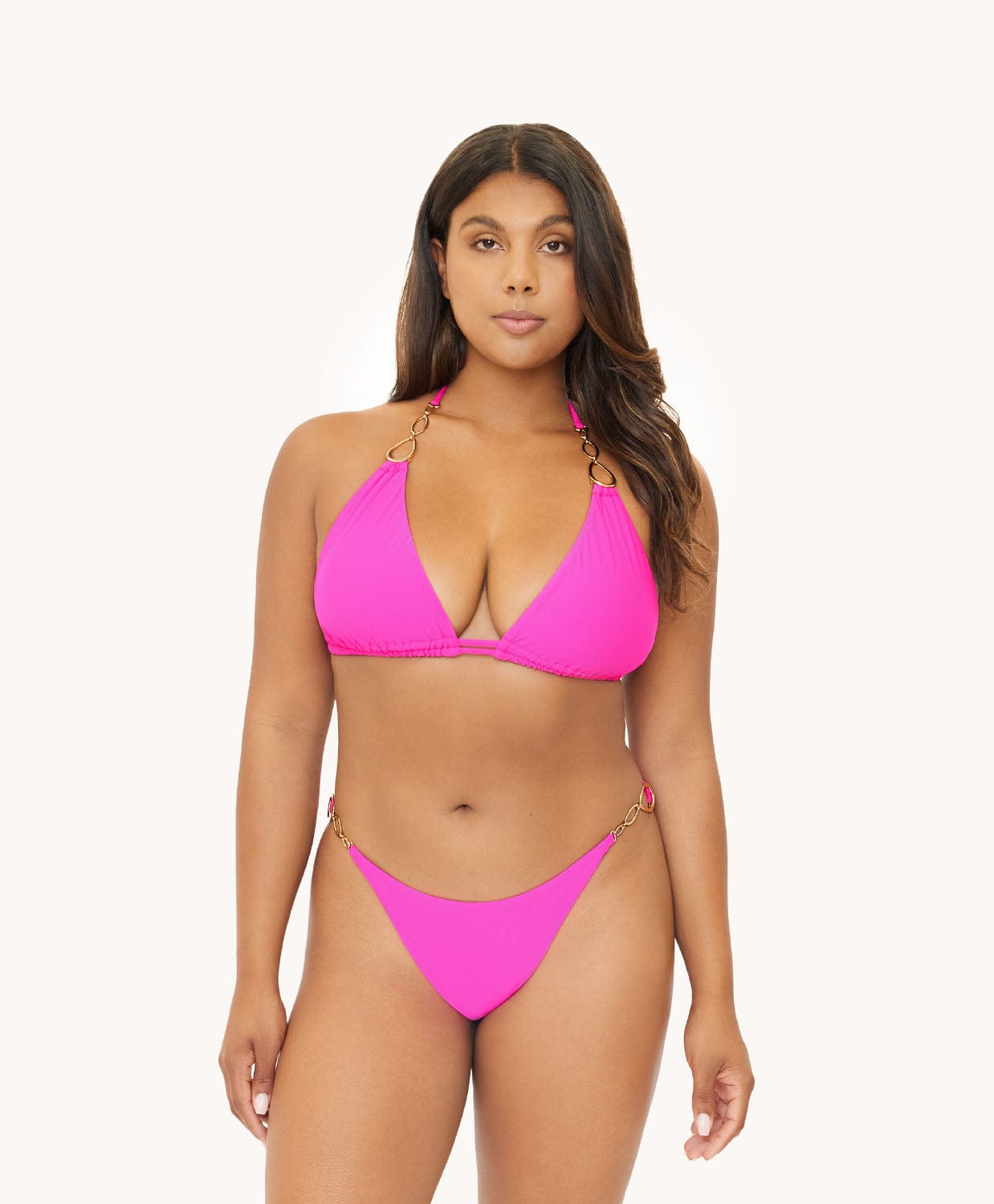 Brunette woman wearing a neon pink bikini in front of a white background.