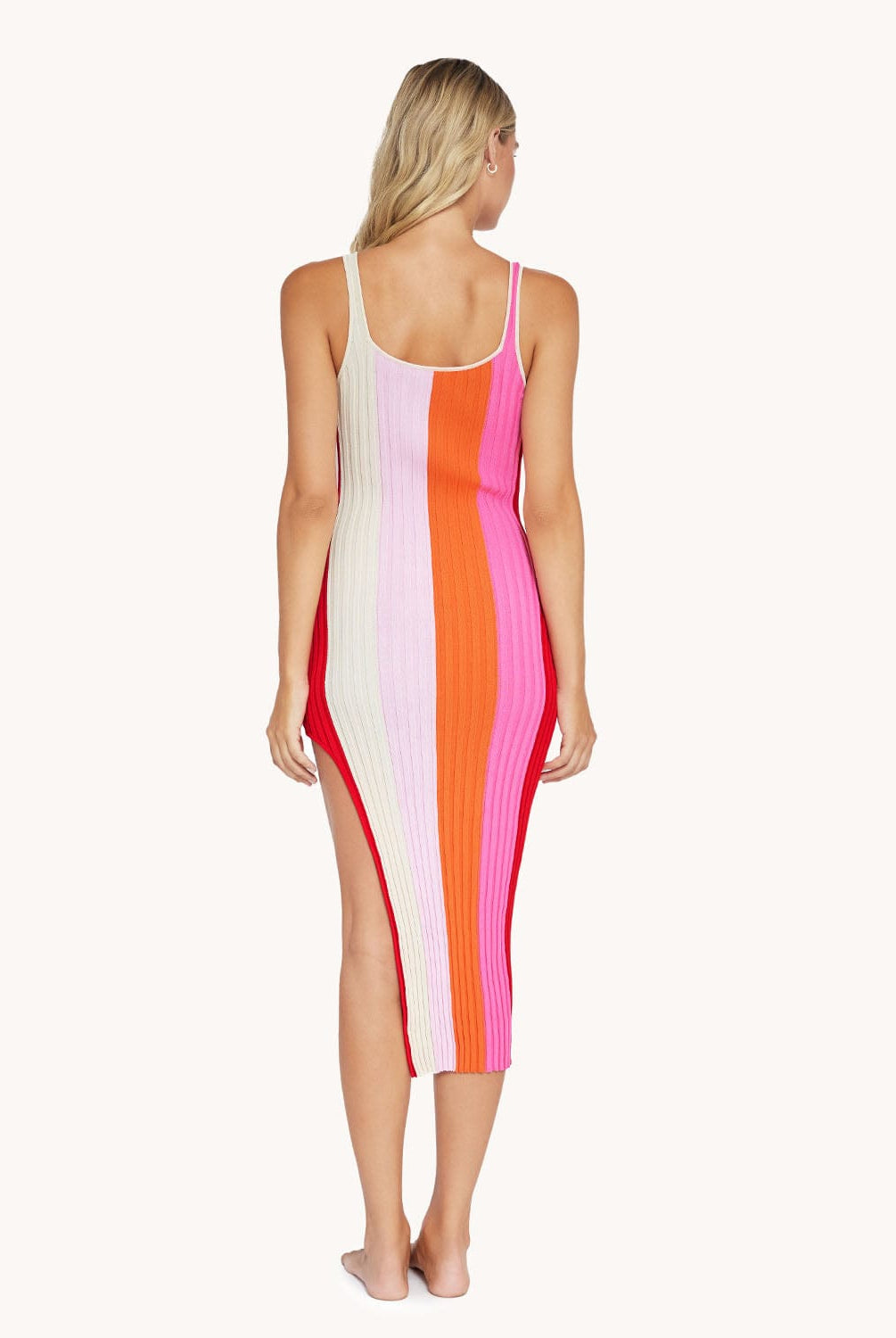 Back view of blonde woman wearing a slit dress in front of a white background.