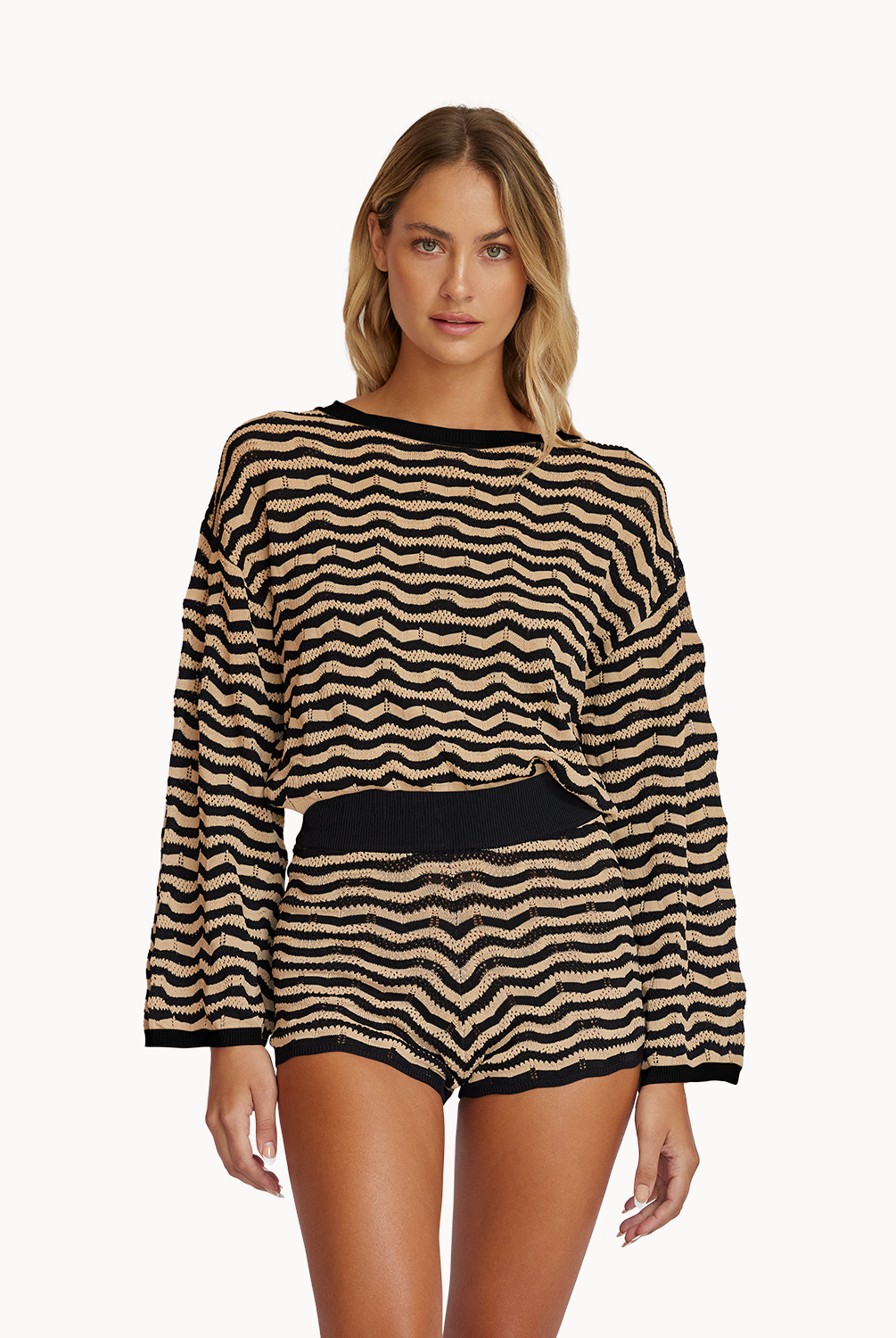 A woman wearing a striped long sleeve top and matching shorts standing against a white wall.