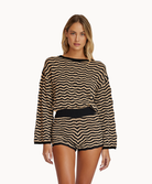 A woman wearing a striped long sleeve top and matching shorts standing against a white wall.