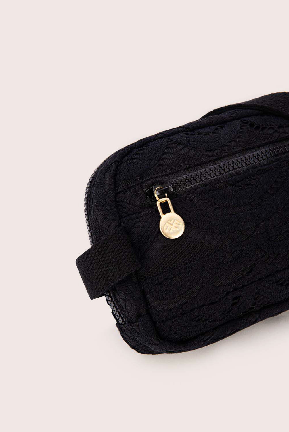 A black lace crossbody bag against a white wall.