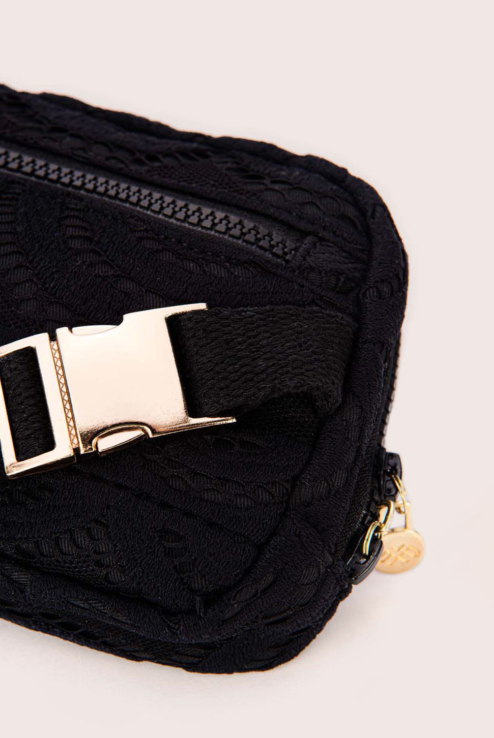 A black lace crossbody bag against a white wall.