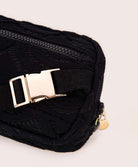 A black lace crossbody bag against a white wall.