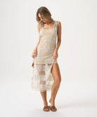 A woman wearing a nude slip dress under a tan crochet dress standing against a white wall.