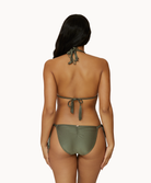 A woman wearing a green bikini facing towards a white wall.