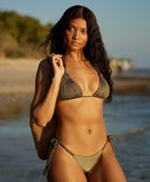A woman wearing a green triangle top bikini standing on the beach near the ocean.