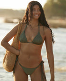 A woman wearing a green triangle top bikini standing on the beach near the ocean.