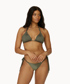 A woman wearing a green bikini standing against a white wall.