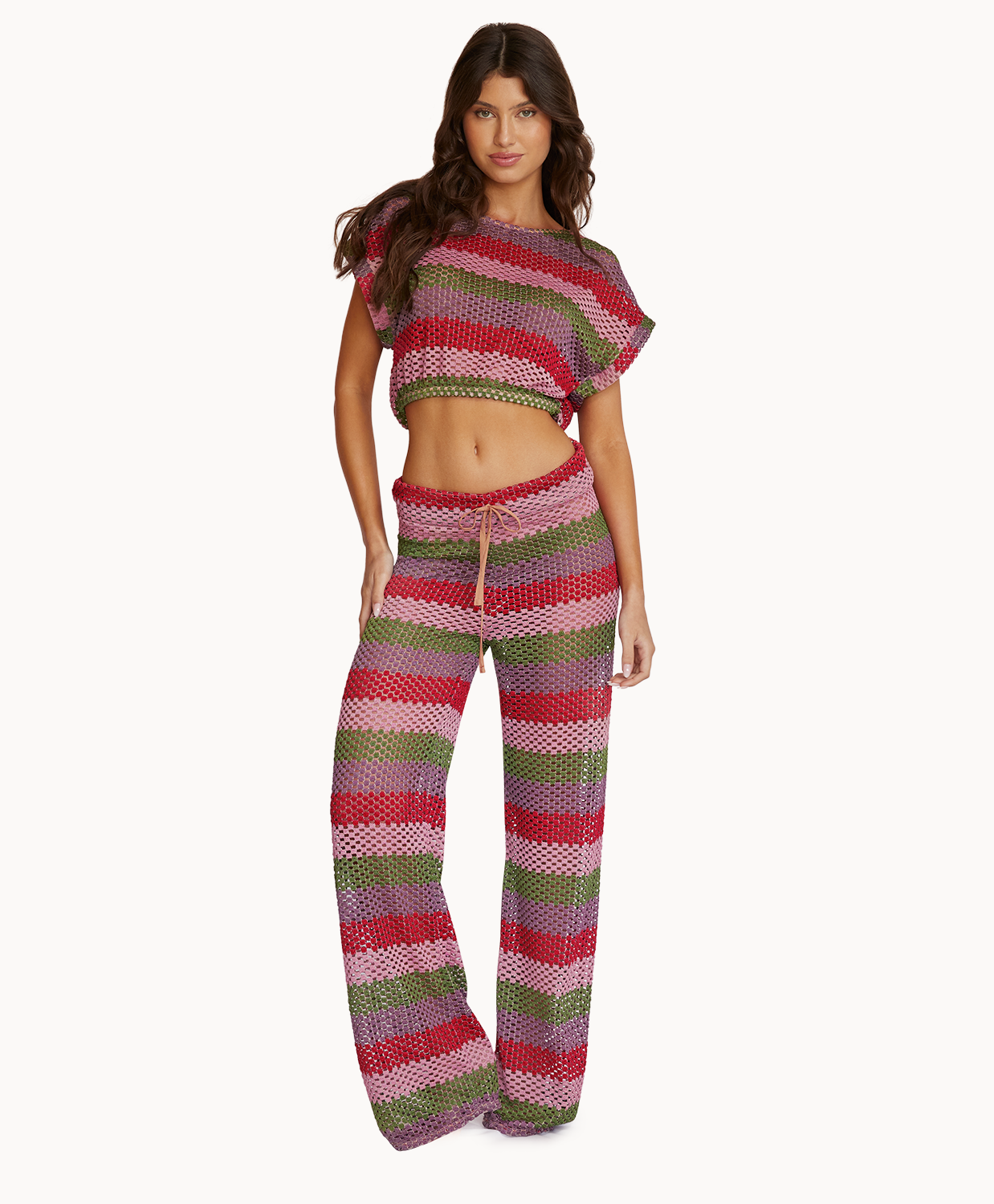 A woman wearing a color block crop top and matching pants standing against a white wall.