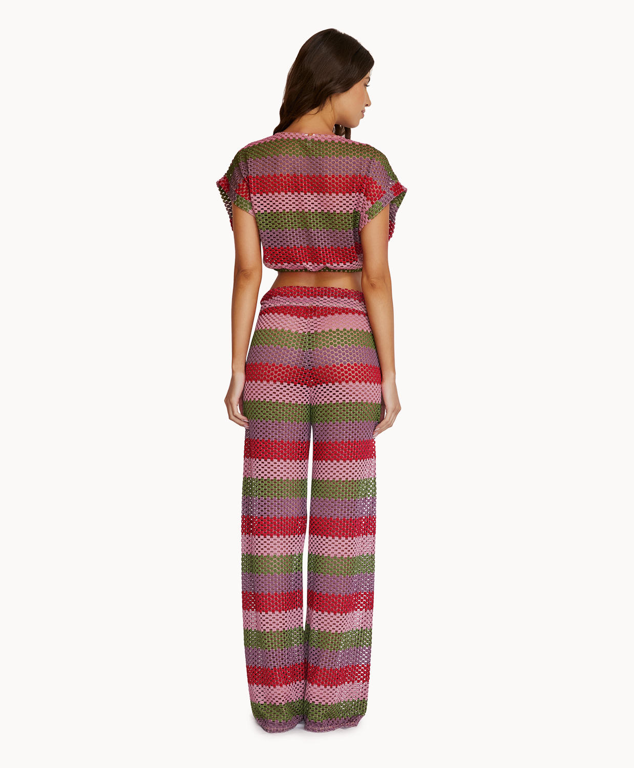 A woman wearing a crochet color block crop top and matching pants facing towards a white wall.