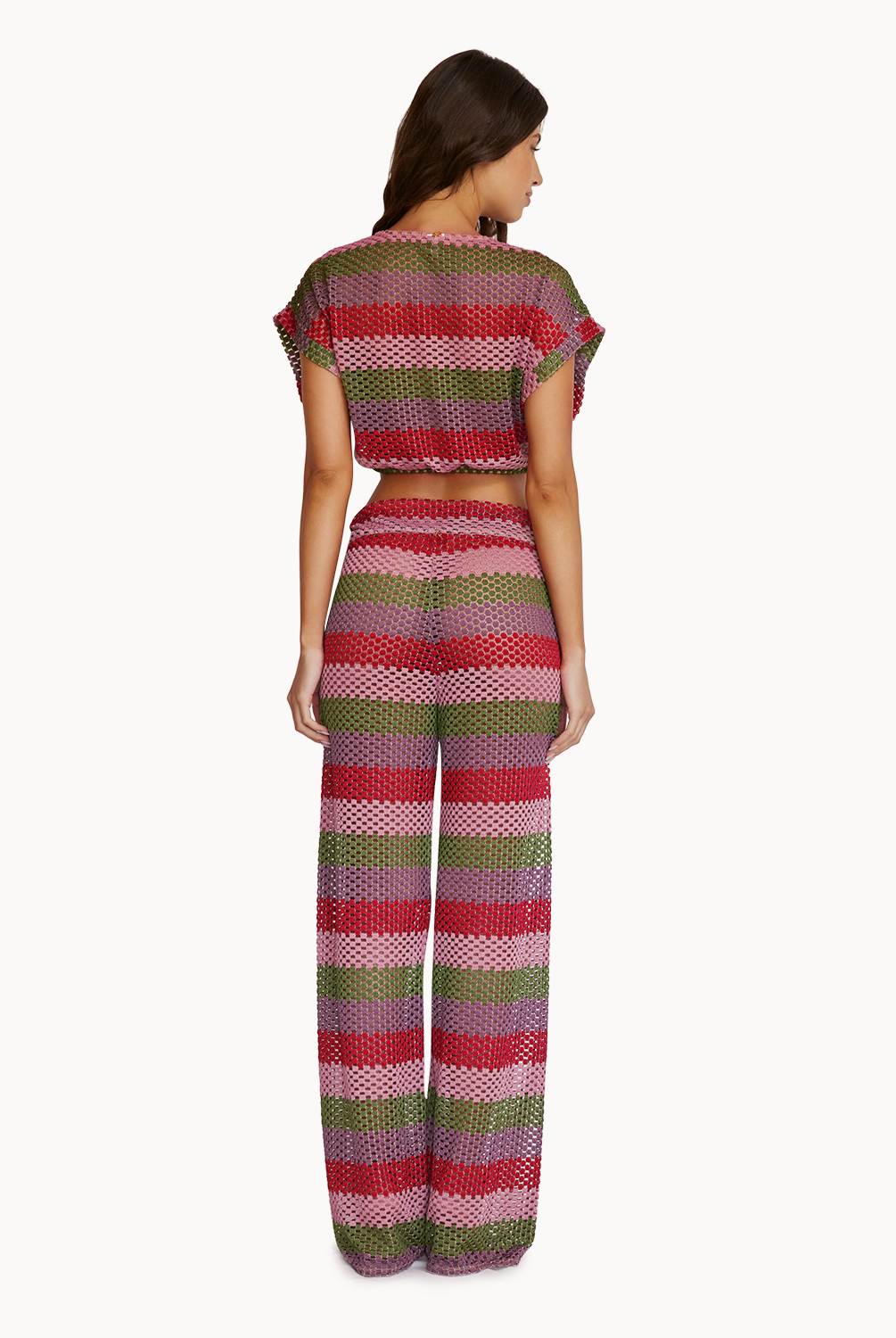 A woman wearing a crochet color block crop top and matching pants facing towards a white wall.