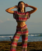 A woman wearing a color block crochet crop top and matching pants standing near the ocean.