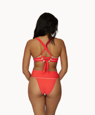 A woman wearing a high waist red bikini facing towards a white wall.