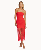 A woman wearing a red strapless mesh dress with fringe standing against a white wall.