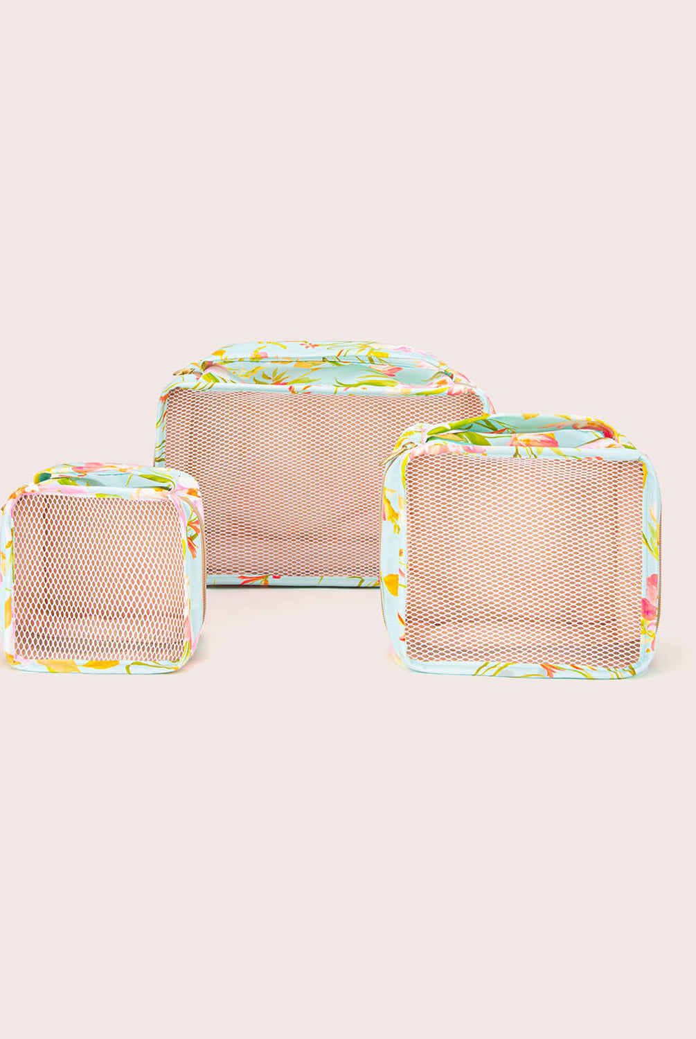 Three mesh packing cubes with floral patterns on a light beige background