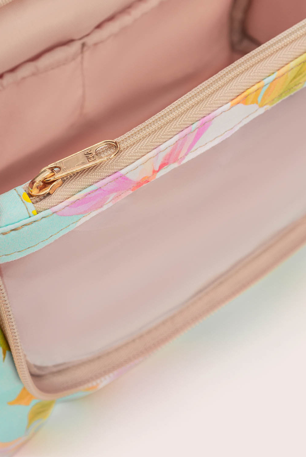 Close-up of a floral-patterned bag with a gold zipper on a light pink background