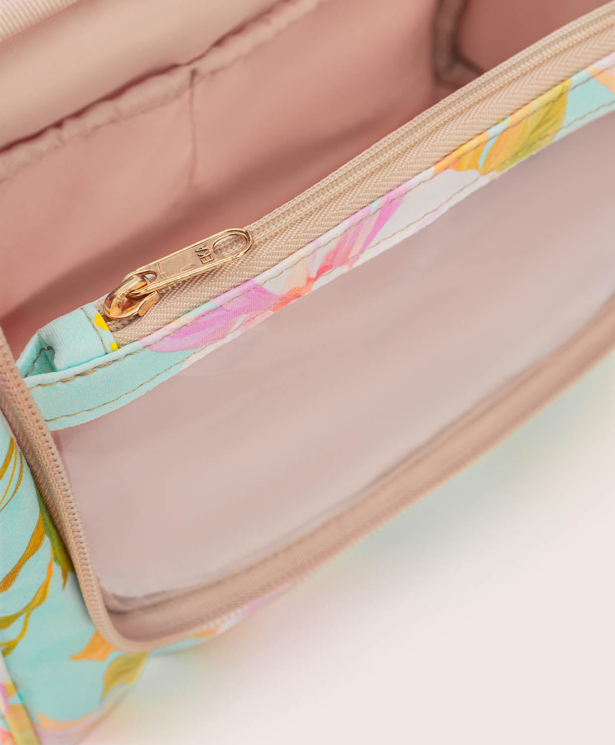 Close-up of a floral-patterned bag with a gold zipper on a light pink background