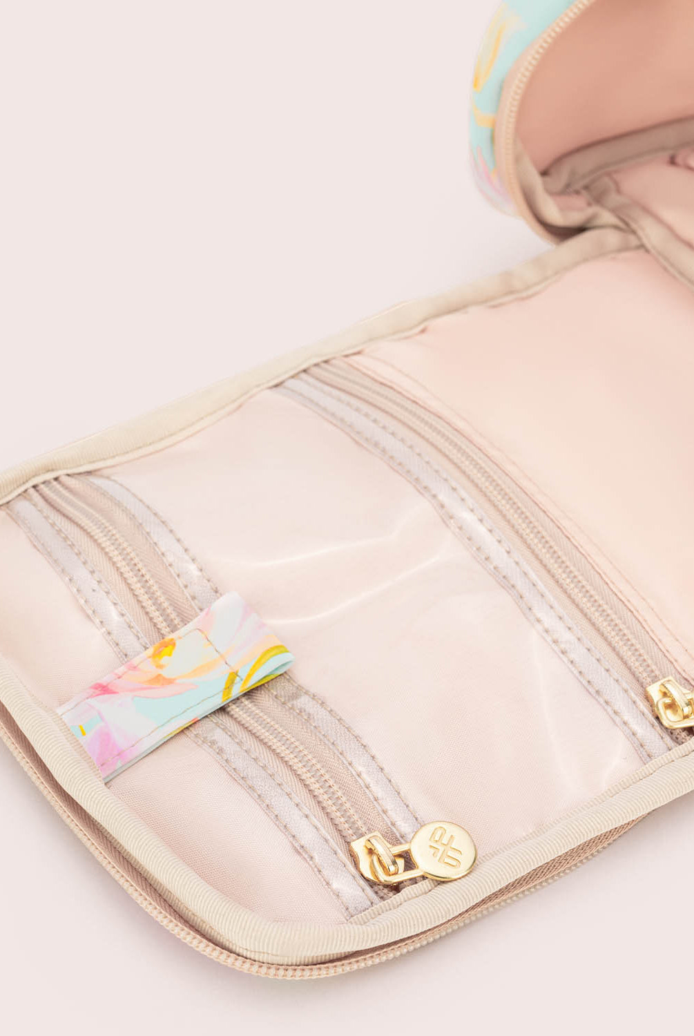 Beige toiletry bag with floral accents on a light pink background