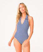 A woman wearing a blue and white striped one piece swim suit standing in front of a white wall.